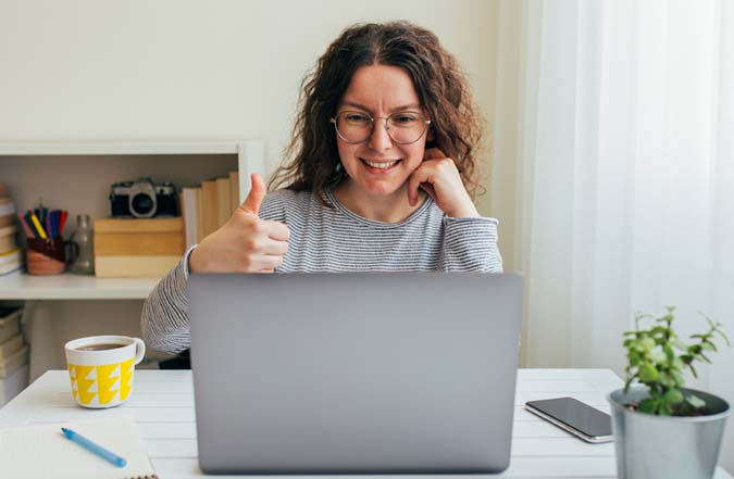 Woman looking at computer giving thumbs-up sign