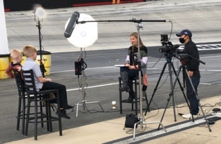 Two children being interviewed and filmed at a racetrack.