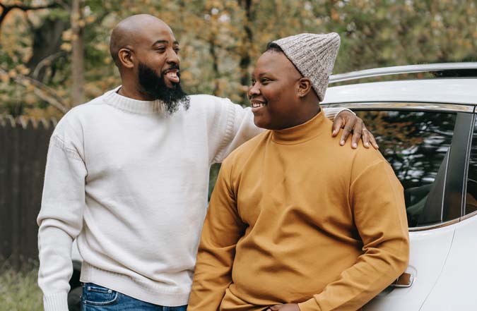 Adult man with arm around teen boy, leaning on car