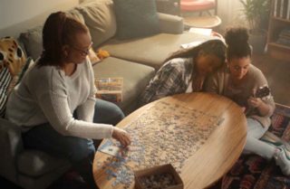 Mother and two teen daughters putting puzzle together in living room.