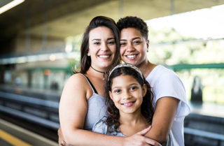 A family smiles and embraces one another at a train station