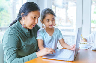 Woman and child sitting at a table and looking at a laptop screen together
