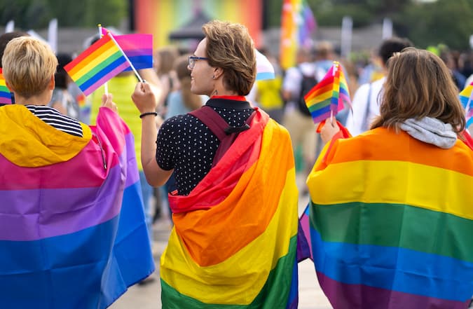 Three people wrapped in bisexual and pride flags celebrating at a Pride event