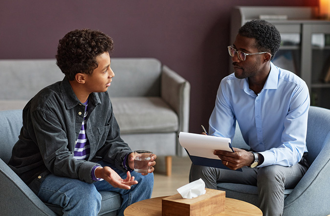 Teenager sitting in an office and speaking with a mental health professional.